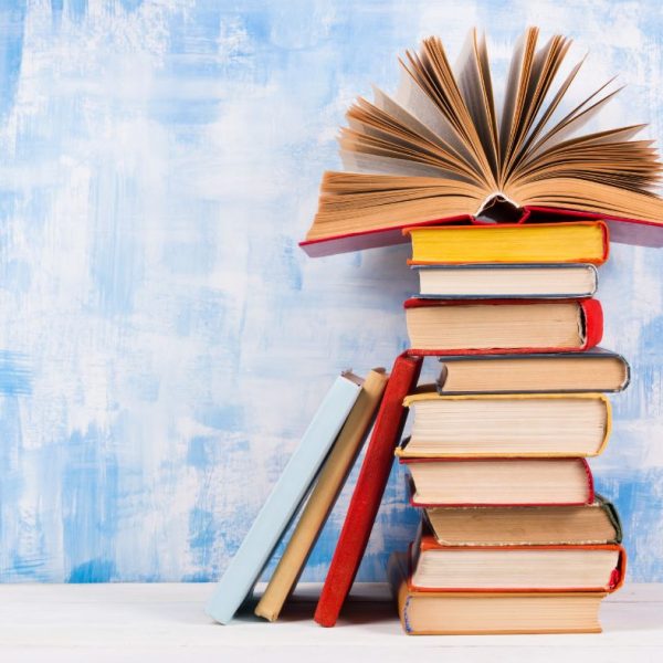 Das Bild zeigt einen Stapel Bücher. Obenauf liegt ein geöffnetes Buch, dessen Seiten sich wie ein Fächer geöffnet haben.