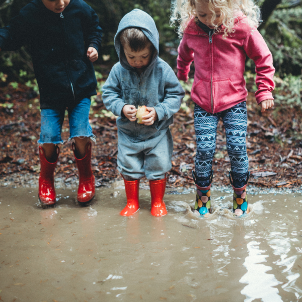 Drei Kinder, die in eine große Pfütze springen.