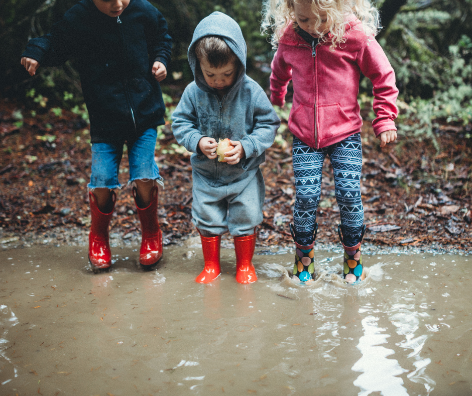 Drei Kinder, die in eine große Pfütze springen.