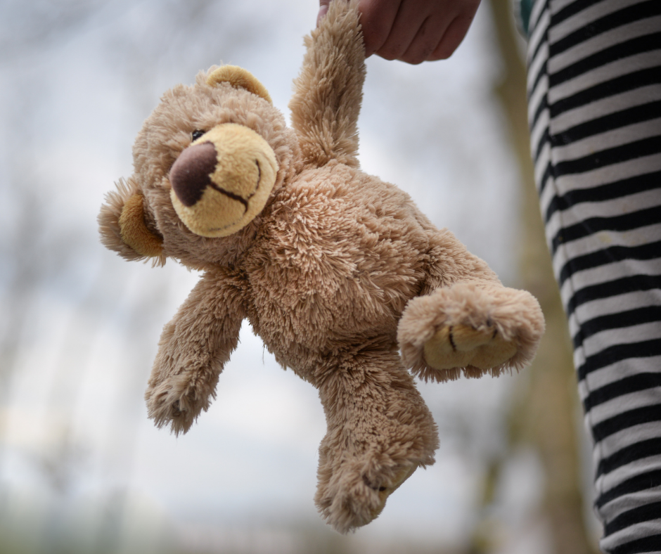 Ein Teddybär baumelt von einer Hand eines Kindes herab, welches einen seiner Arme in der Hand hält.